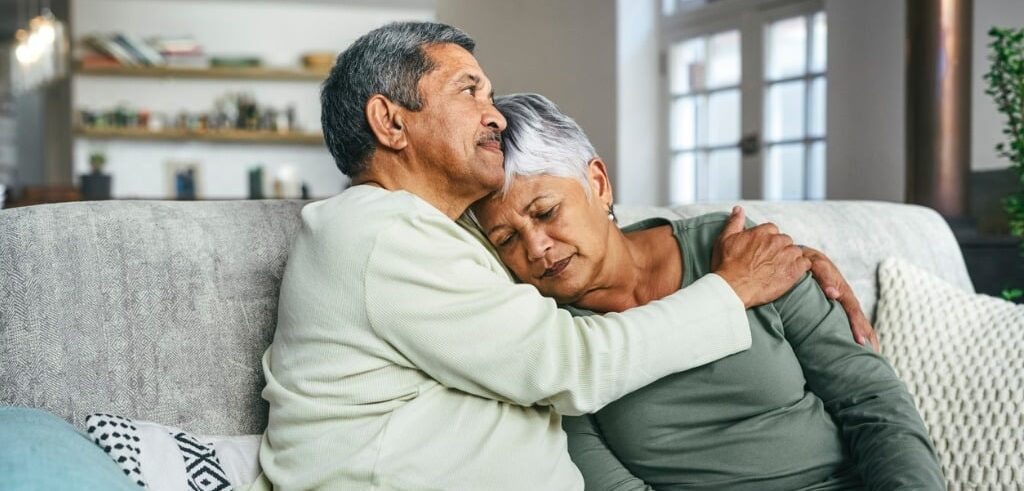 elderly man comforting his depressed wife on a couch