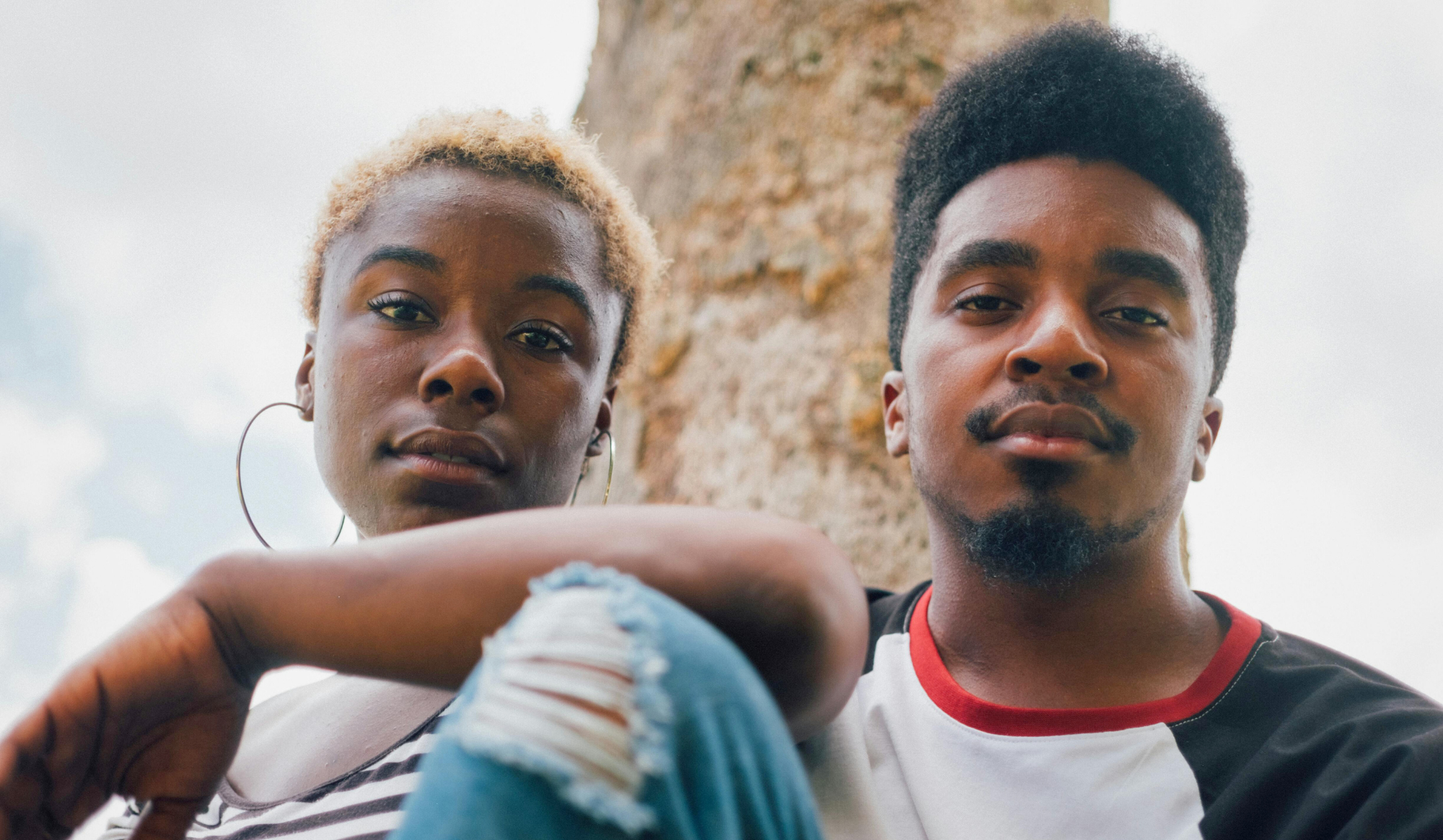 Two young black adults are sitting next to eachother and looking at the camera.